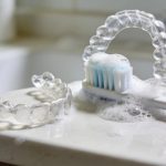 Clear aligners and toothbrush on a bathroom counter highlighting daily cleaning routines for optimal oral hygiene